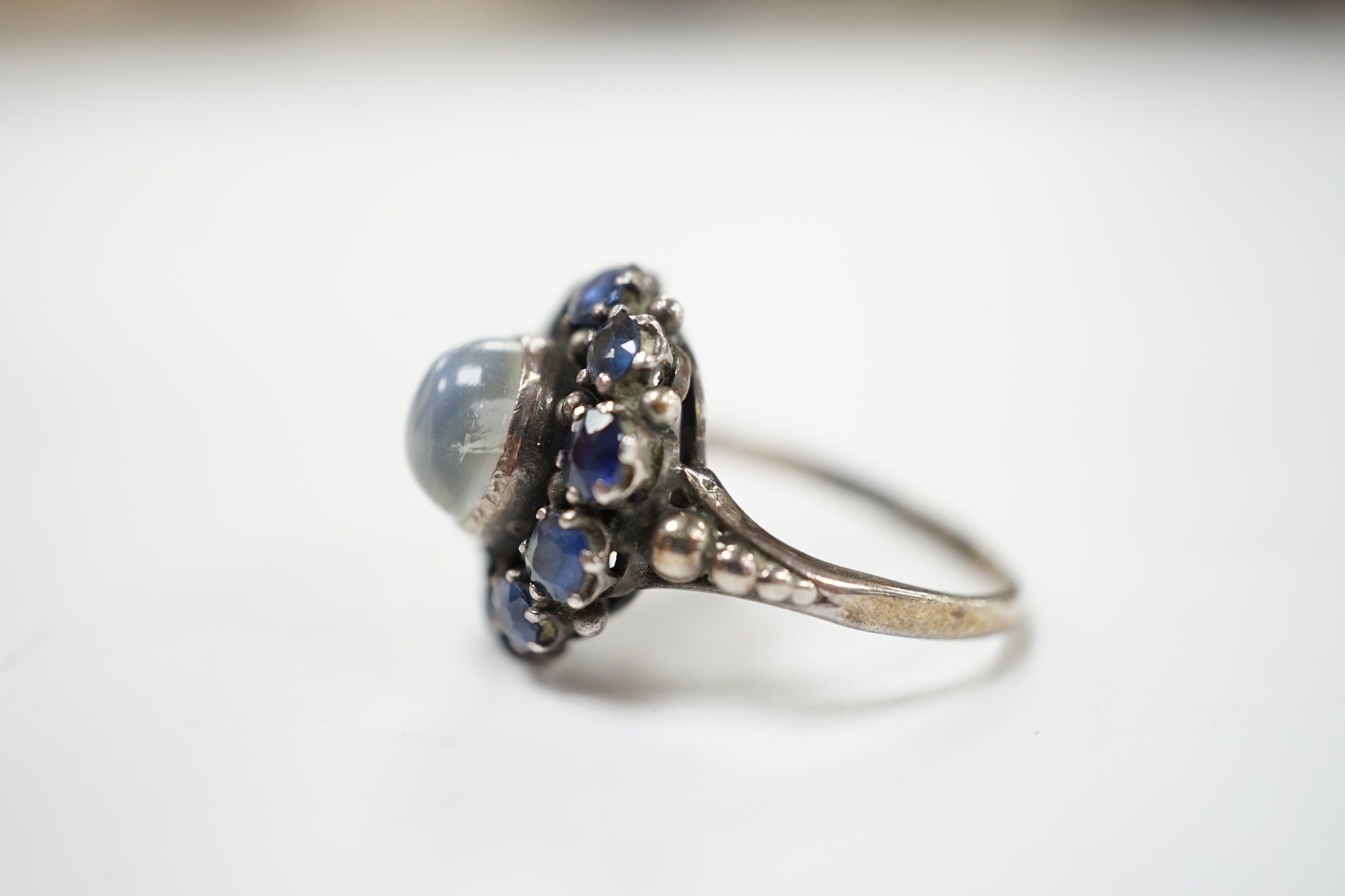 An Arts & Crafts white metal, moonstone and sapphire set circular cluster ring, in the manner of Sibyl Dunlop, size M. Condition - fair